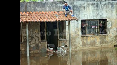 La imagen de la desazón: un hombre sobre el techo de su casa resignado y a la espera de que el agua termine de bajar. (LA OPINION)