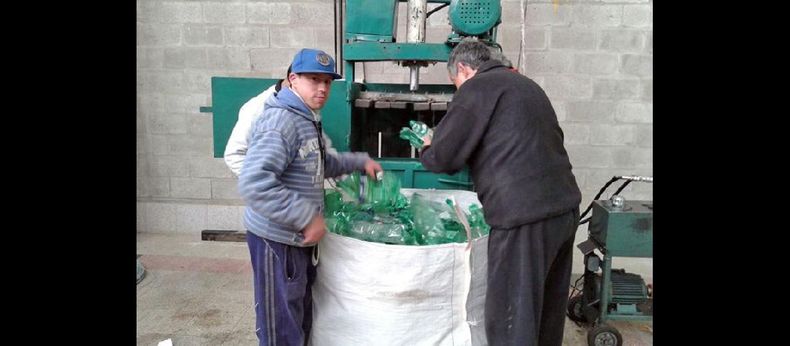 Los chicos que asisten al Taller Protegido colaboran con quien dirige la prensa hidráulica, proceso con el que se aplastan las botellas. (FACEBOOK TALLER PROTEGIDO PERGAMINO)